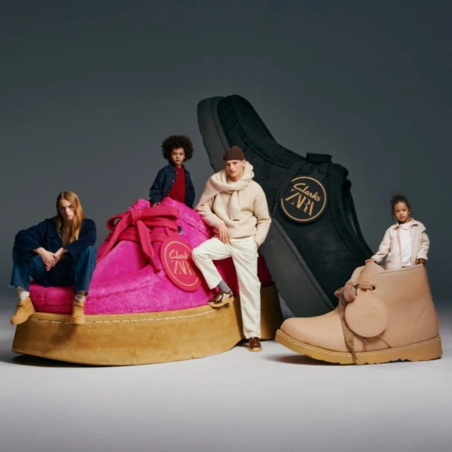 People sit on and stand by giant shoes for Clarks and Zara clothing and shoe collaboration against a gray studio background.