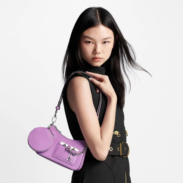 Elegant Asian woman showcases a lavender Louis Vuitton handbag, wearing a stylish black sleeveless dress against a clean white backdrop.