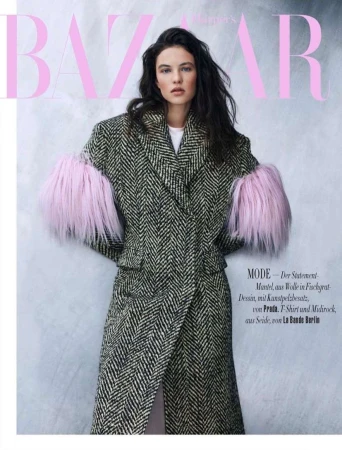 Fashion editorial shot of a woman wearing a black and white herringbone coat with pink fur sleeves against a light pink backdrop.