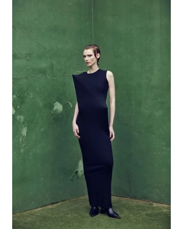Model in a structured black dress standing against a mottled green wall photographed by Marcin Tyszka.