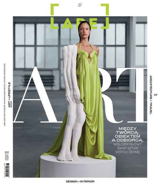 Magazine cover featuring a woman in a green dress posing with a sculpture in a minimalist indoor setting with natural lighting.