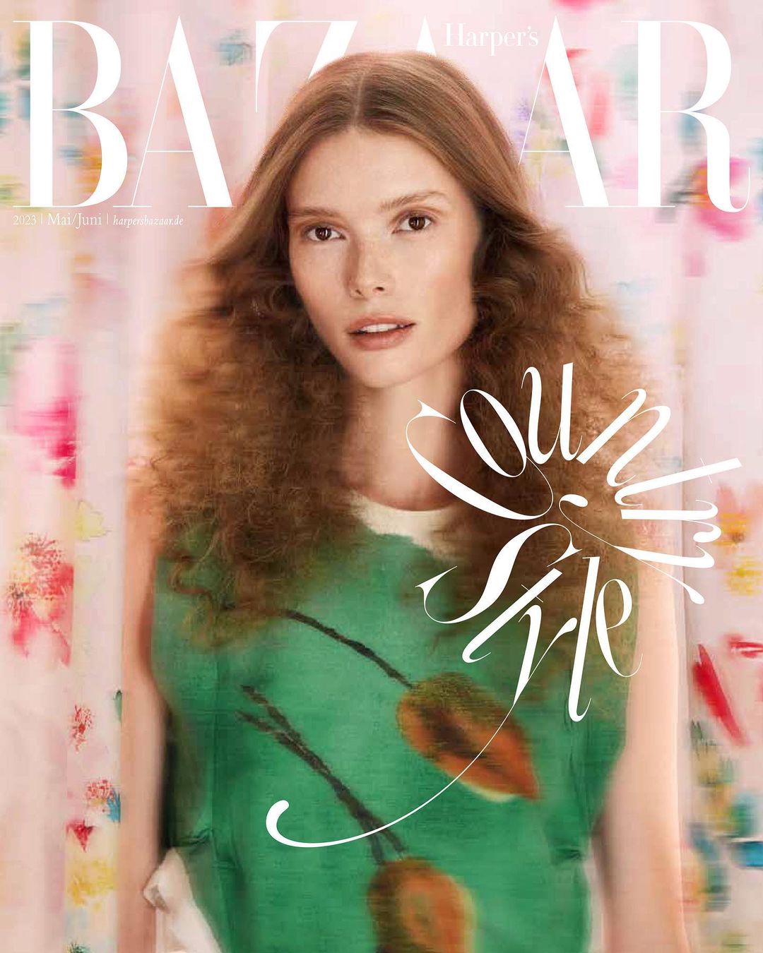 Fashion magazine cover featuring a model with long, wavy auburn hair, wearing a green floral top, against a blurred floral backdrop.