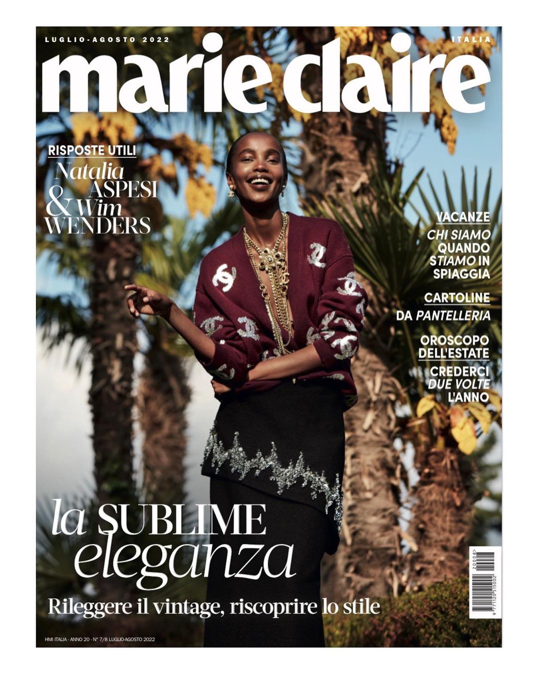 Magazine cover featuring a smiling woman with a maroon sweater, ornate necklace, and patterned skirt, posing against a leafy background.