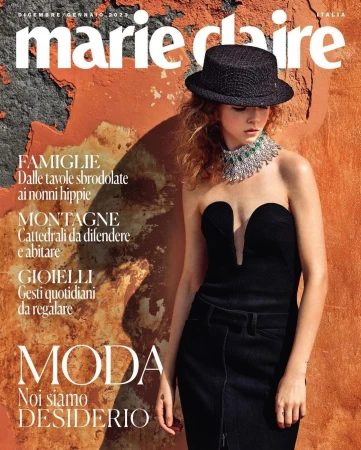 Model wearing black strapless dress, black hat, and ornate silver necklace against textured orange wall by Marcin Tyszka