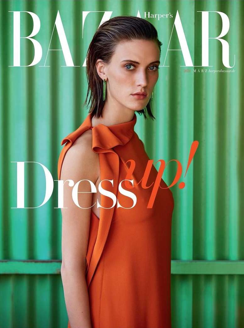 Magazine cover featuring a woman in an orange dress against a green corrugated metal background, showcasing a blend of fashion and editorial style.