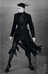 Monochrome fashion portrait of a model in a black blazer and fringed skirt standing outdoors on paved ground