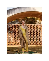 Model in yellow lace top and beige trench coat holding a coiled hose outdoors in Milan, photographed by Marcin Tyszka.