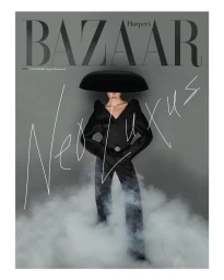 Model in structured black outfit with wide brim hat and smoke at feet against grey background for Harper's Bazaar