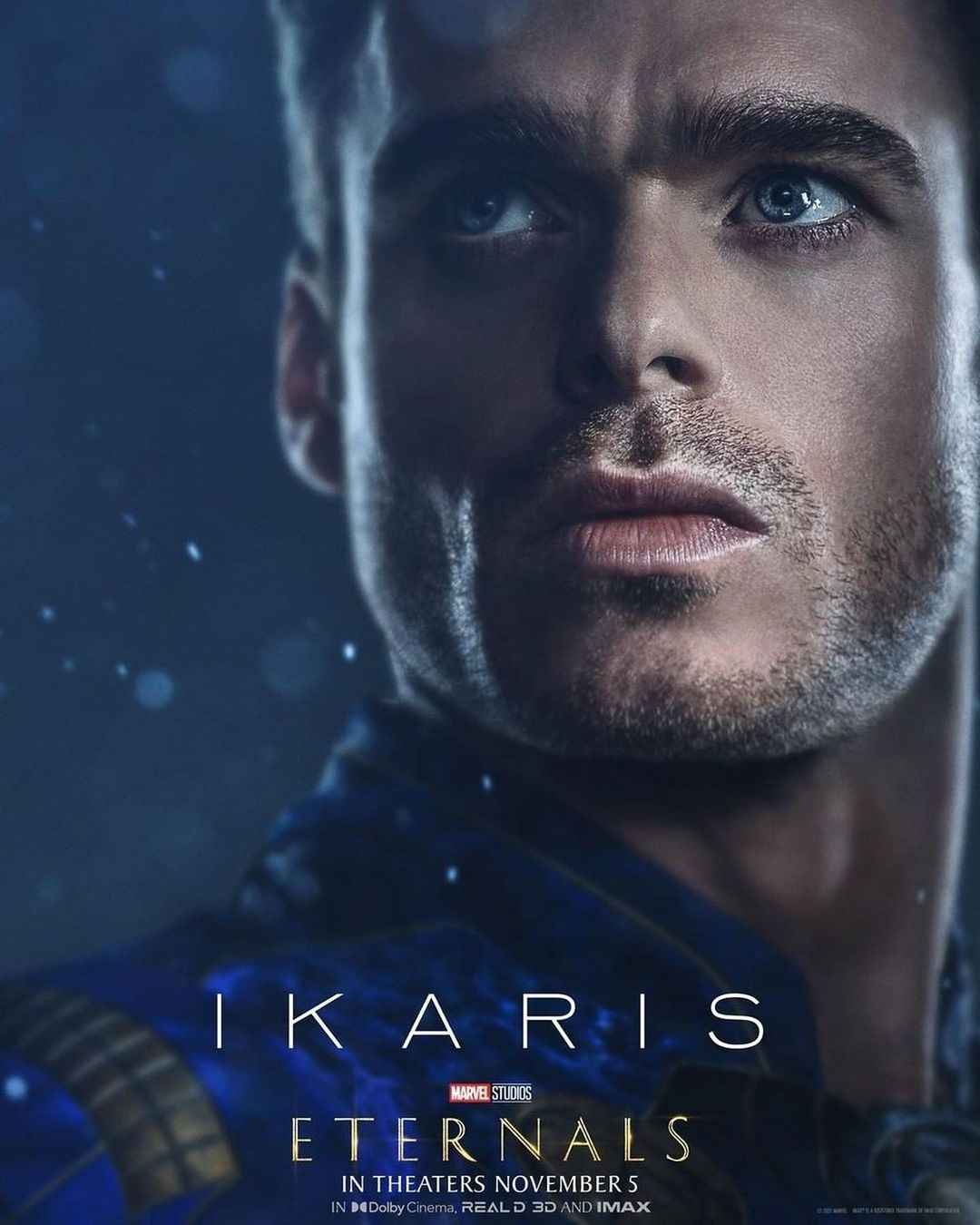 Close-up of Richard Madden in Marvel's Eternals movie poster, showcasing a blue and gold costume against a dark, bokeh-lit background.