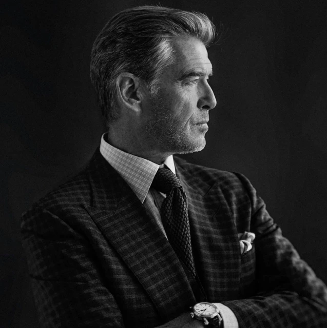 Profile portrait of adult male with graying hair wearing a suit, tie, and watch against a dark background in black and white.