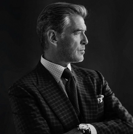 Profile portrait of adult male with graying hair wearing a suit, tie, and watch against a dark background in black and white.