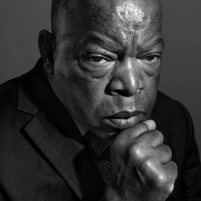 Black and white portrait of an adult male in a suit and tie, looking thoughtfully at the camera with his chin resting on his hand.