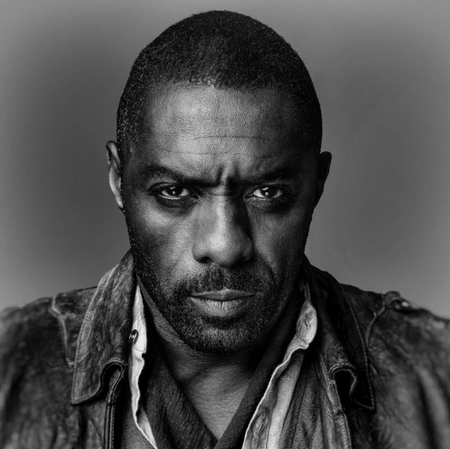 Portrait of Idris Elba in black and white, showcasing his intense gaze, textured skin, and the details of his worn leather jacket.