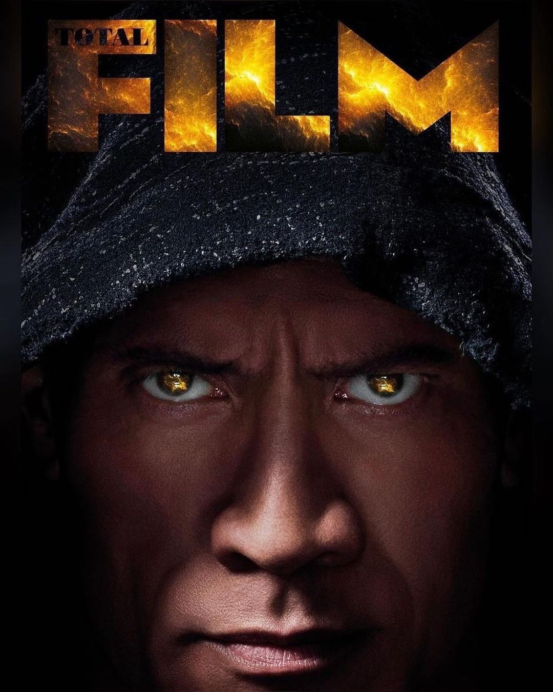 Close-up portrait of a hooded adult male with intense golden eyes set against a black background with glowing 'TOTAL FILM' text.