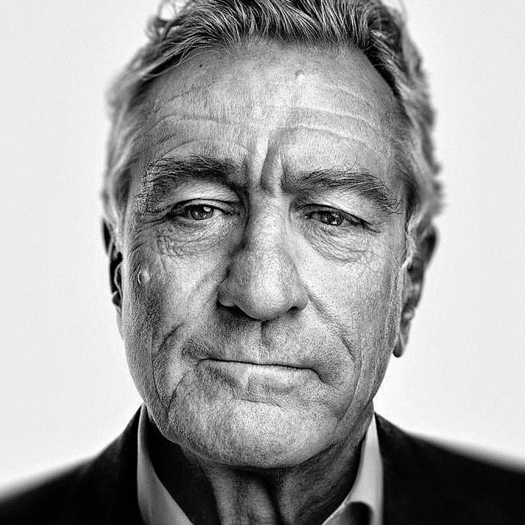 Close-up black and white portrait of an elderly man in a suit, focusing on his face with wrinkles and a neutral expression.