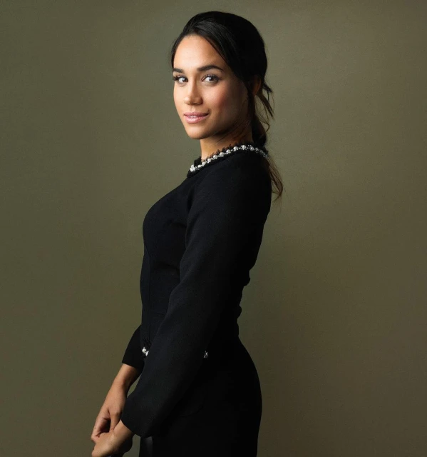 Portrait of a woman in a black long-sleeved dress with pearl detailing, looking at the camera in a studio setting with soft lighting.
