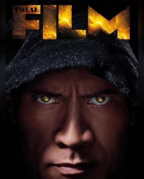 Close-up portrait of Dwayne Johnson wearing a dark hooded garment with glowing golden light reflected in his eyes, by Marco Grob