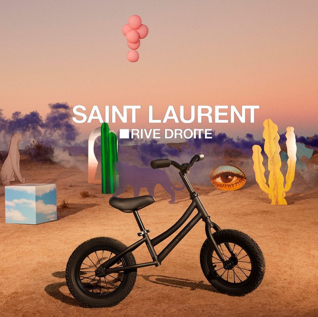 Black child's bicycle in a surreal desert landscape, featuring colorful geometric shapes, abstract sculptures, and clear sky in background.