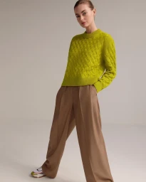 Model in chartreuse cable-knit sweater and wide-leg brown trousers against a neutral background
