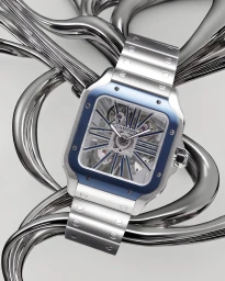 Close-up of a silver wristwatch with a blue bezel resting on abstract metallic sculptural forms against a neutral background.