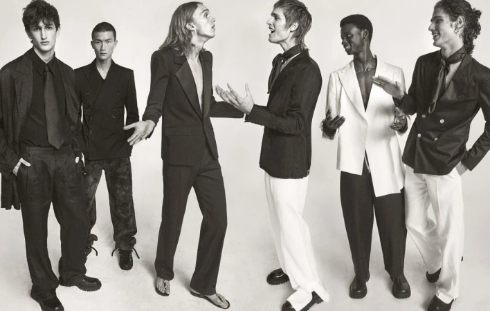 Six fashion models pose in formal wear in a black-and-white studio shot, showcasing a variety of blazers, suits, and elegant styles.