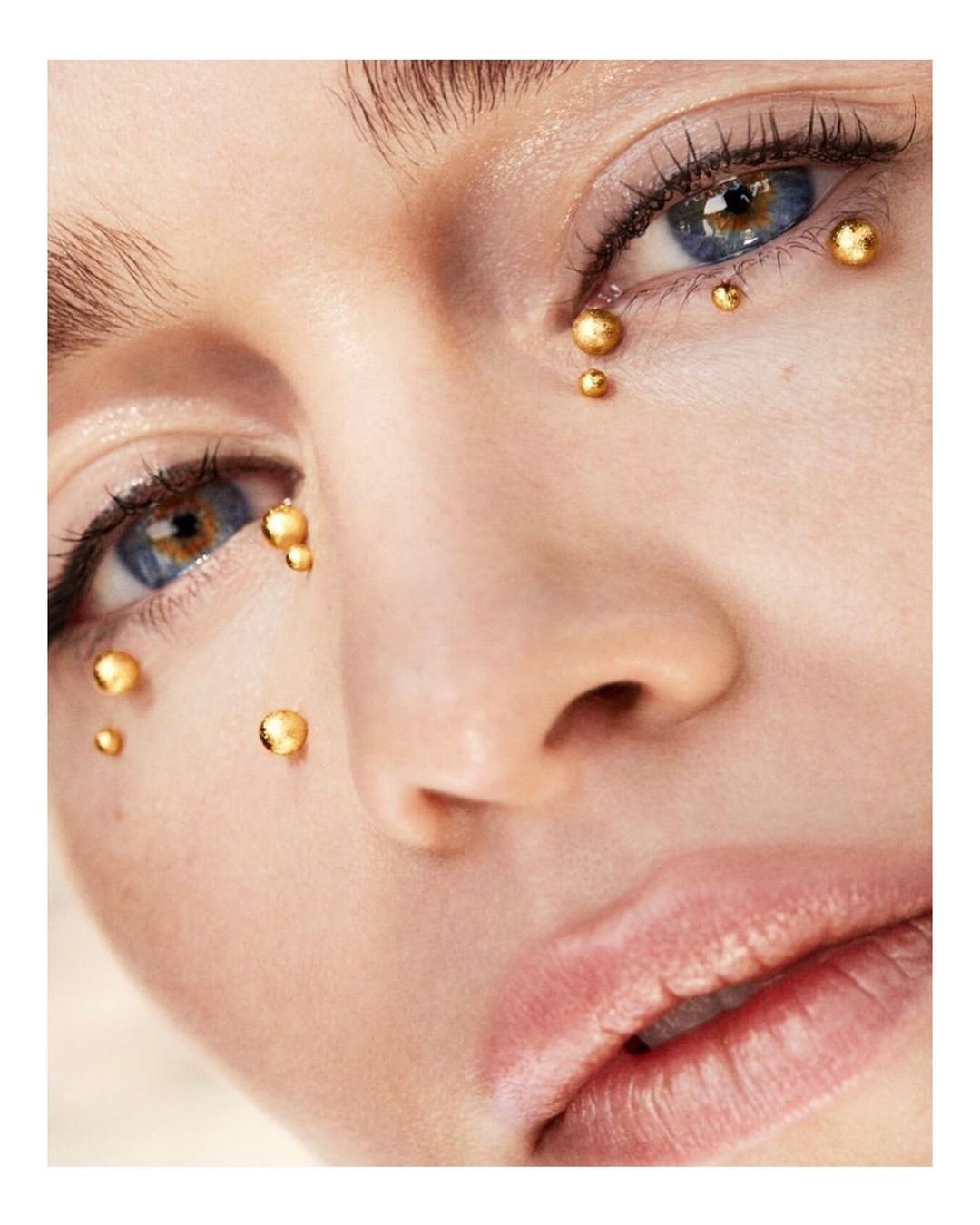 Close-up of a woman's face with gold bead makeup around the eyes. Beauty shot featuring light skin and blue eyes.