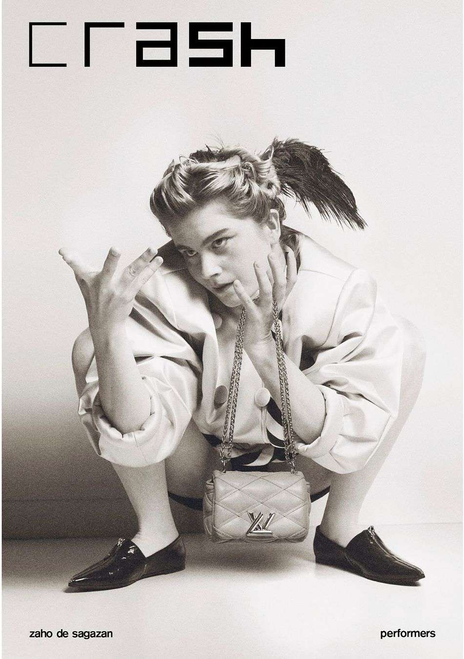 Black and white fashion magazine cover featuring a model squatting with a Louis Vuitton purse, wearing a jacket and flats.