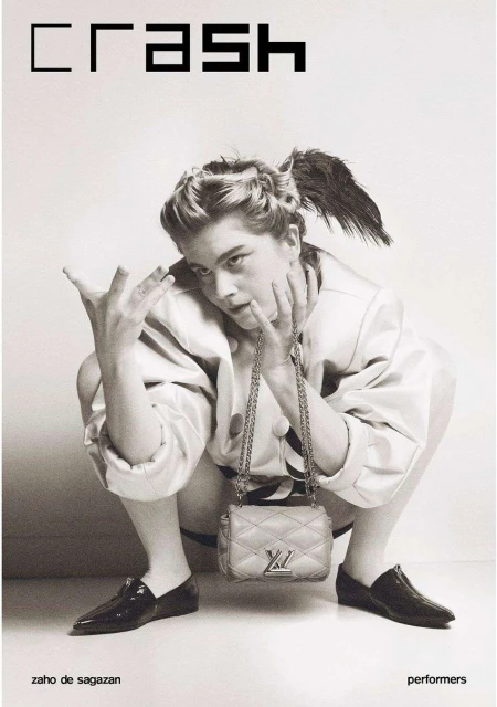 Black and white fashion magazine cover featuring a model squatting with a Louis Vuitton purse, wearing a jacket and flats.