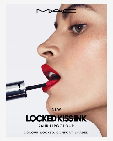 Close-up of a woman's face applying vibrant red lipstick with a brush, emphasizing the color and makeup texture against a bright background.
