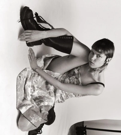 Model wearing a floral dress and black boots sitting against a white seamless background in New York.