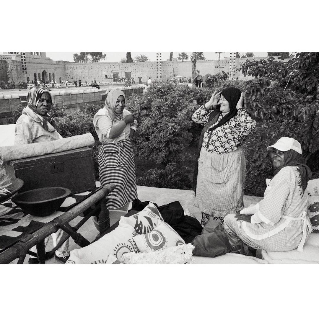 Black and white image of four women in headscarves, aprons, and casual clothing standing outdoors near trees and a building.