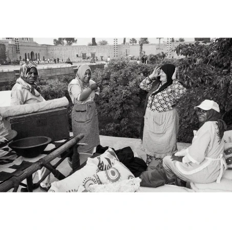 Black and white image of four women in headscarves, aprons, and casual clothing standing outdoors near trees and a building.