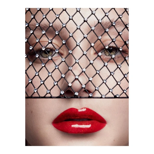 Close-up portrait of a fair-skinned adult female with glossy red lips, wearing a sparkling black mesh face covering, fashion, beauty.