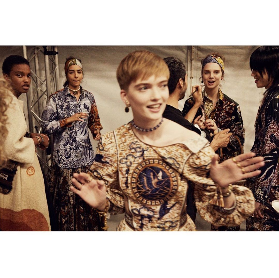 Backstage view of a diverse group of fashion models in patterned tops and headscarves, gathered at a fashion show event.