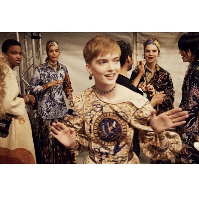 Backstage view of a diverse group of fashion models in patterned tops and headscarves, gathered at a fashion show event.