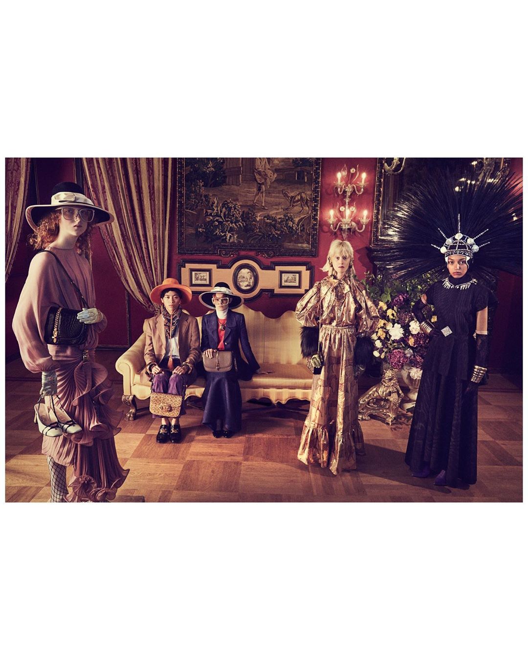Group of five people in vintage-inspired fashion, posing in an ornate indoor setting with floral arrangements and antique furniture.