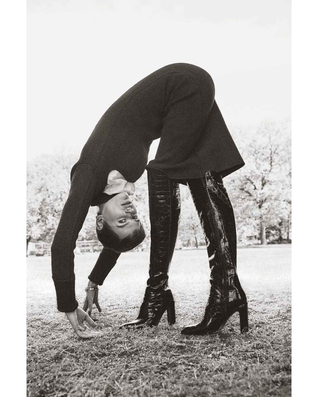 Model bending backwards upside down in a park wearing a dark dress and tall black boots, photographed by Marcus Ohlsson