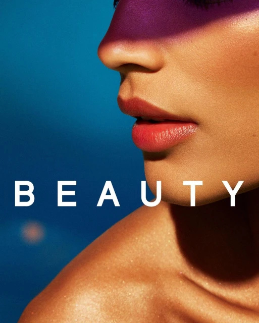 Close-up studio shot of an adult female with red lipstick and purple eyeshadow, set against a blue backdrop with the word 'BEAUTY' visible.