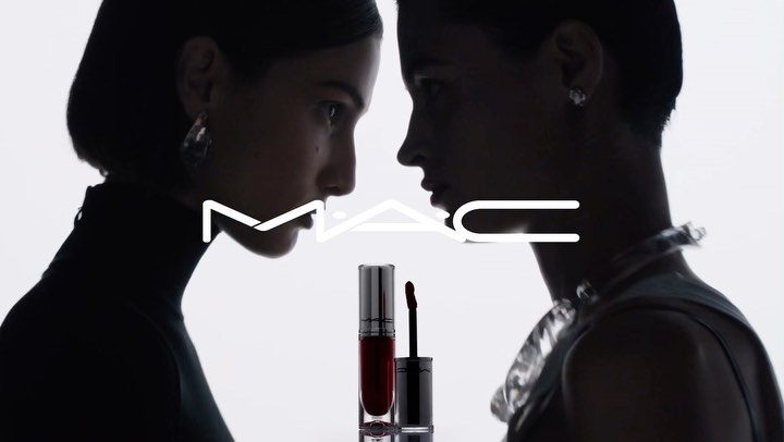 Two adult females and a lipstick product in a beauty-focused shot with a white background and the MAC Cosmetics logo.