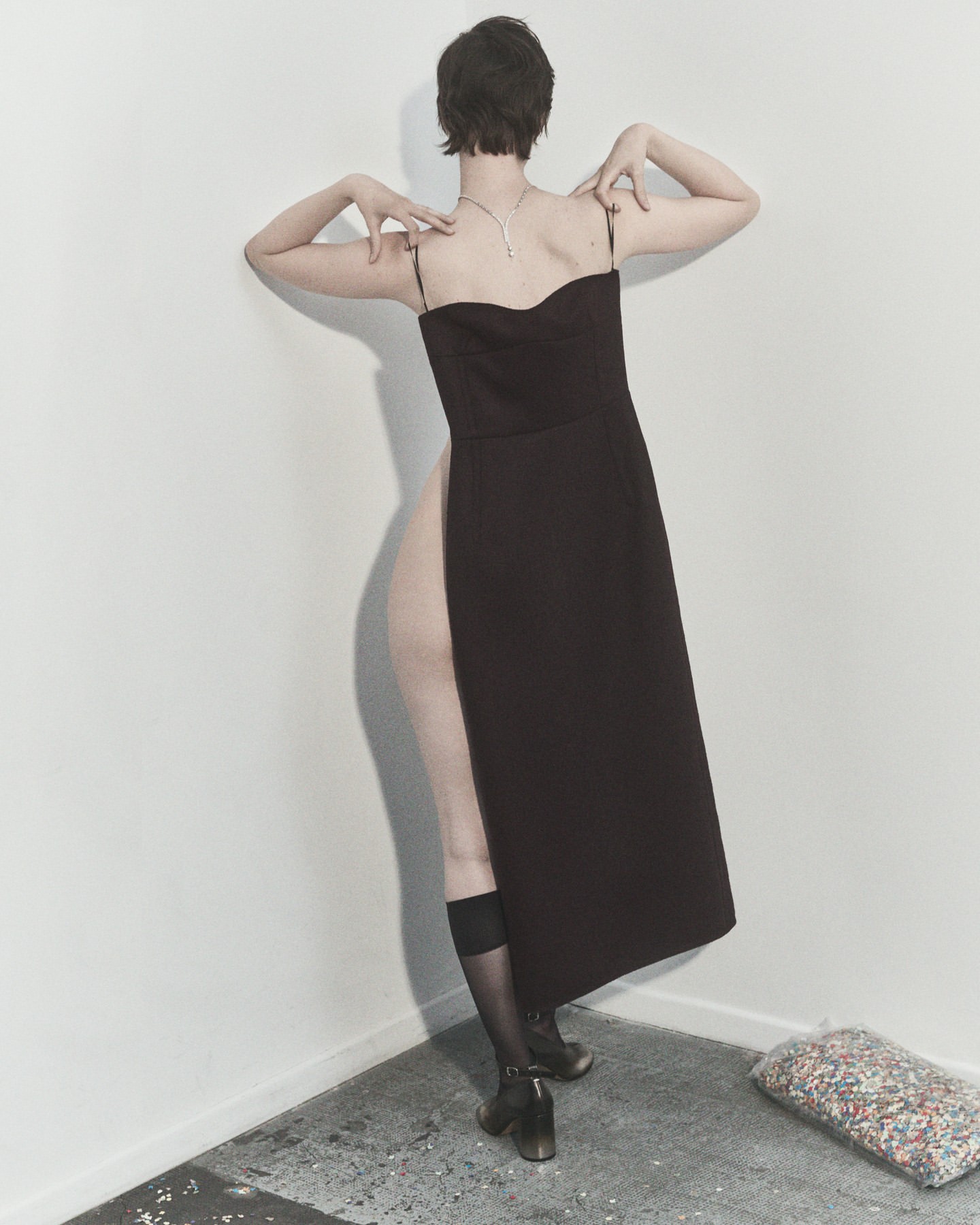 Woman in elegant black dress, seen from the back, poses in a minimalist studio with geometric lines, showcasing fashion and style.