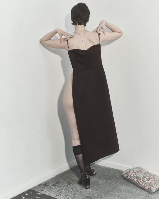 Woman in elegant black dress, seen from the back, poses in a minimalist studio with geometric lines, showcasing fashion and style.