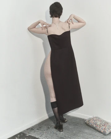 Woman in elegant black dress, seen from the back, poses in a minimalist studio with geometric lines, showcasing fashion and style.