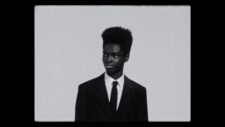 Portrait of a black man wearing a dark suit and tie against a plain light background, captured with heavy film grain.