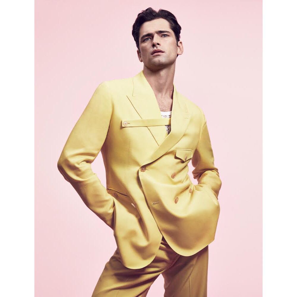 Man in yellow double-breasted suit poses in front of pink backdrop in studio lighting, showcasing fashion and portrait photography.