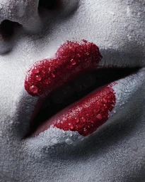 Extreme close-up of lips covered in vibrant red lipstick and white powder with droplets of water on a textured surface.
