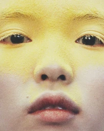 Extreme close-up portrait of a person face covered in yellow powder with dark eyes and natural lips by Marcus Ohlsson