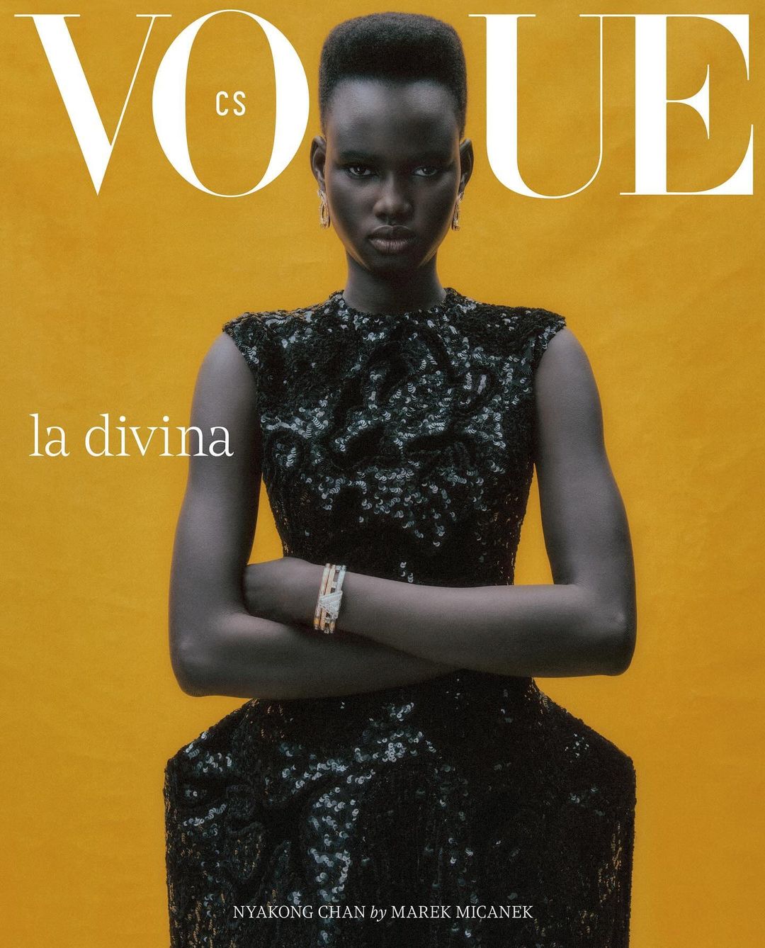 Vogue cover featuring Nyakong Chan in a dark, glittering dress against a golden backdrop, arms crossed, with bold magazine typography.