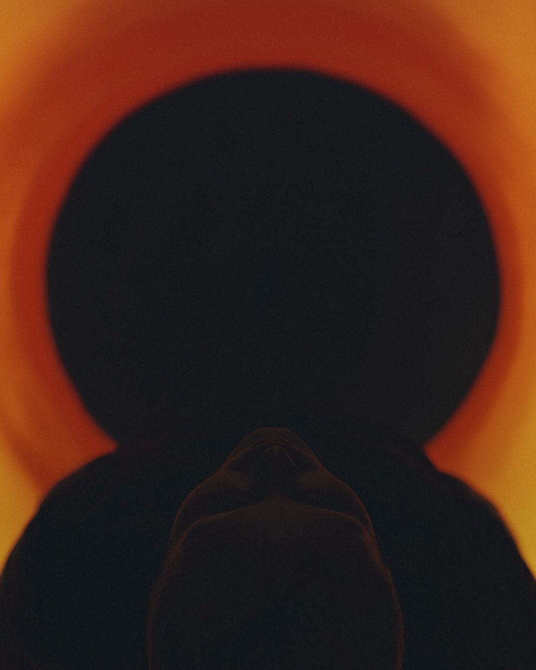 Silhouette of a person's head against a vibrant orange and black background, creating a dramatic and mysterious visual.