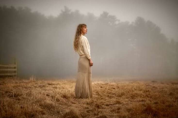 Woman with long blonde hair in a cream sweater and skirt standing in a foggy field by Margaret Lampert