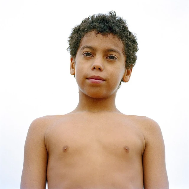 Portrait of a young boy with curly hair looking directly at the camera against a bright white background in a studio setting.
